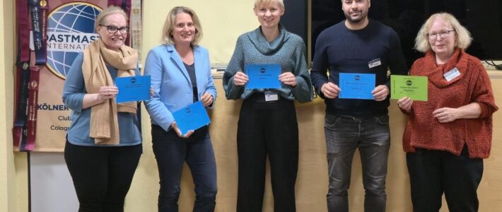 Fünf Mitglieder der Kölner Sprechbar stehen nebeneinander im Bürgerzentrum Deutz und halten ihre farbigen Auszeichnungen aus der Preisverleihung des Abends in die Kamera.