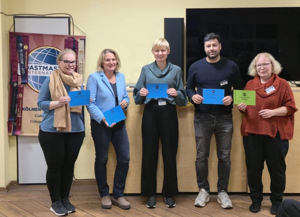 Fünf Mitglieder der Kölner Sprechbar stehen nebeneinander im Bürgerzentrum Deutz und halten ihre farbigen Auszeichnungen aus der Preisverleihung des Abends in die Kamera.