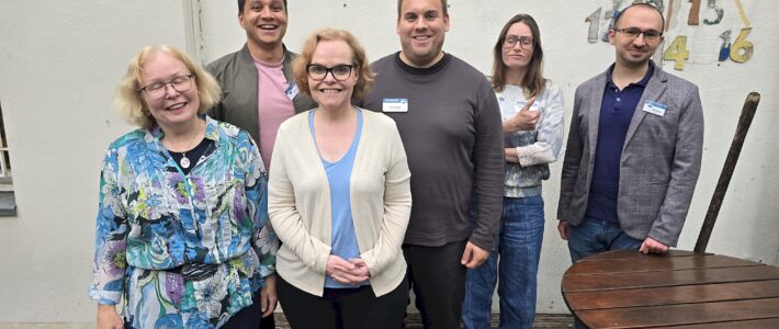 Sechs Mitglieder des neu gewählten Vorstands der Kölner Sprechbar stehen lächelnd in einem Innenhof vor einer hellen Wand. Von links: Andrea Hoffmann, René Benjamin, Sarah Bahß, Kristof Glienke, Danja Krahe und Aleksandr Anfilofev. Ioanna Alexoudi und Sarah Mewes sind nicht im Bild.