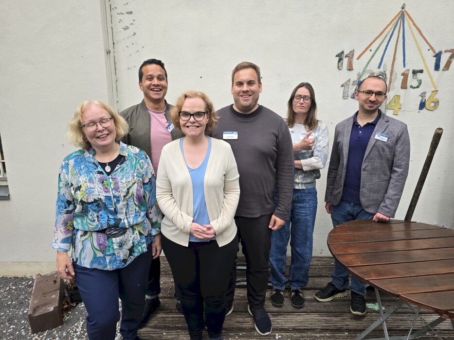 Sechs Mitglieder des neu gewählten Vorstands der Kölner Sprechbar stehen lächelnd in einem Innenhof vor einer hellen Wand. Von links: Andrea Hoffmann, René Benjamin, Sarah Bahß, Kristof Glienke, Danja Krahe und Aleksandr Anfilofev. Ioanna Alexoudi und Sarah Mewes sind nicht im Bild.