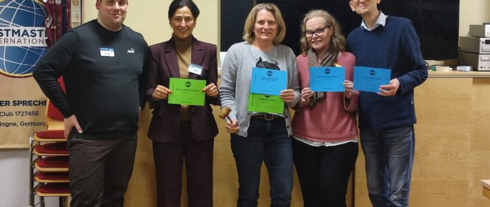 Fünf Mitglieder der Kölner Sprechbar mit Urkunden vor dem Toastmasters-Banner beim Clubabend am 11.03.2026.