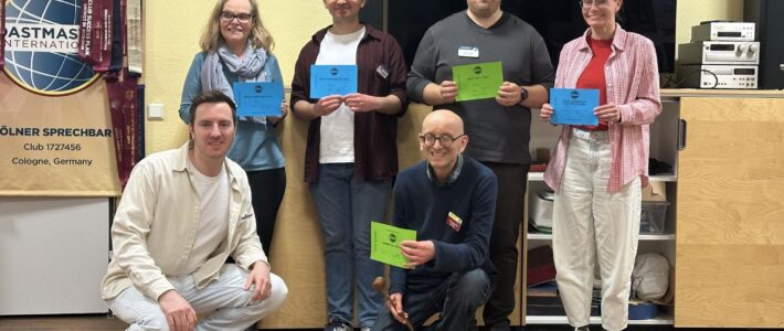 Kölner Sprechbar | Gestrandet gestartet, reich an Erfahrungen zurückgekehrt 🏝️ | Rückblick auf den Clubabend vom 15.04.2026 Sechs Mitglieder der Kölner Sprechbar mit Urkunden vor dem Toastmasters-Banner beim Clubabend am 15.04.2026.