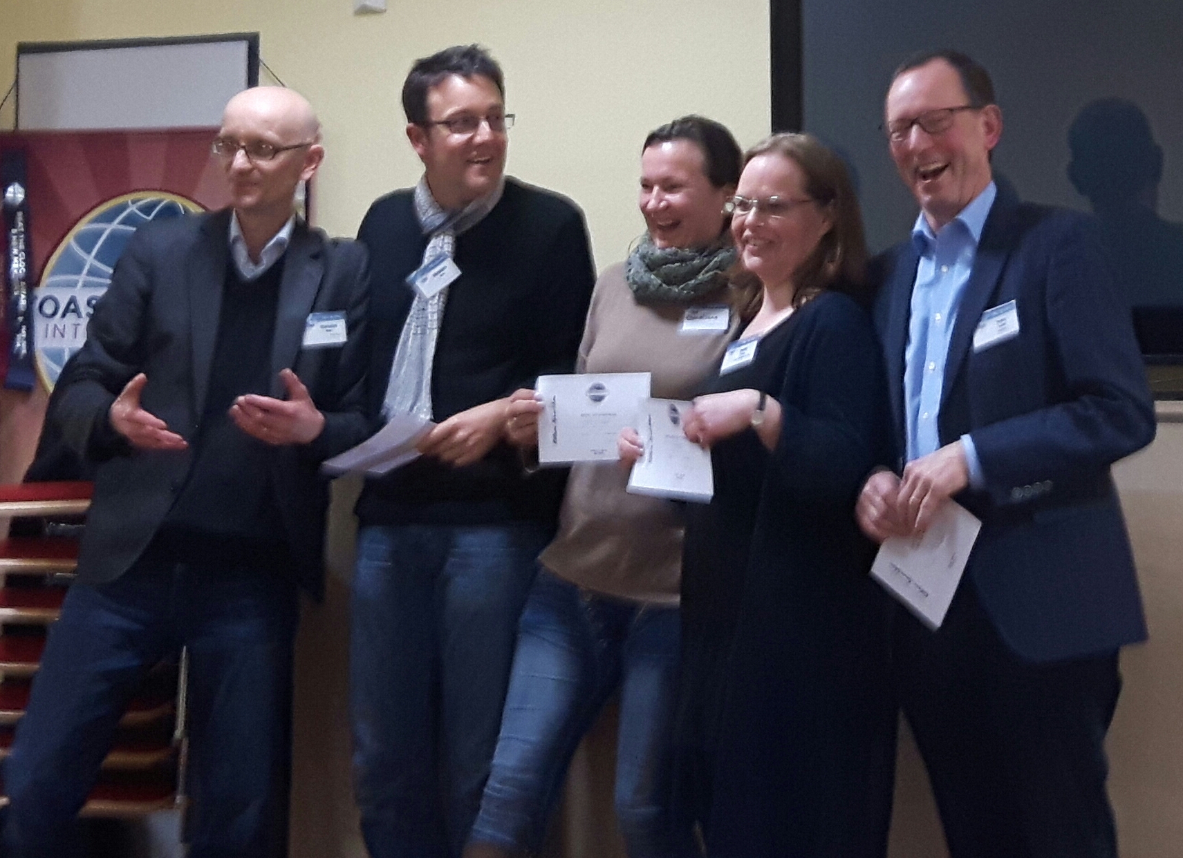 Mitglieder der Kölner Sprechbar lachen mit Urkunden in der Hand vor dem Toastmasters-Banner beim Clubabend am 10.02.2016.