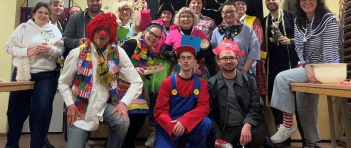 Kölner Sprechbar: Karnevals-Clubabend am 11.02.2026 – Redelust trifft Rhetorik 🎭🎤 Eine große Gruppe der Kölner Sprechbar in bunten Karnevalskostümen posiert lachend für ein Gruppenfoto im Clubraum.