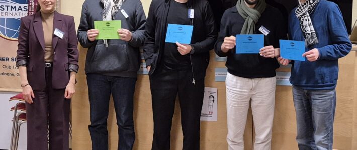 Eine Frau im Anzug und vier Personen mit Urkunden stehen nebeneinander vor dem Toastmasters-Banner der Kölner Sprechbar.