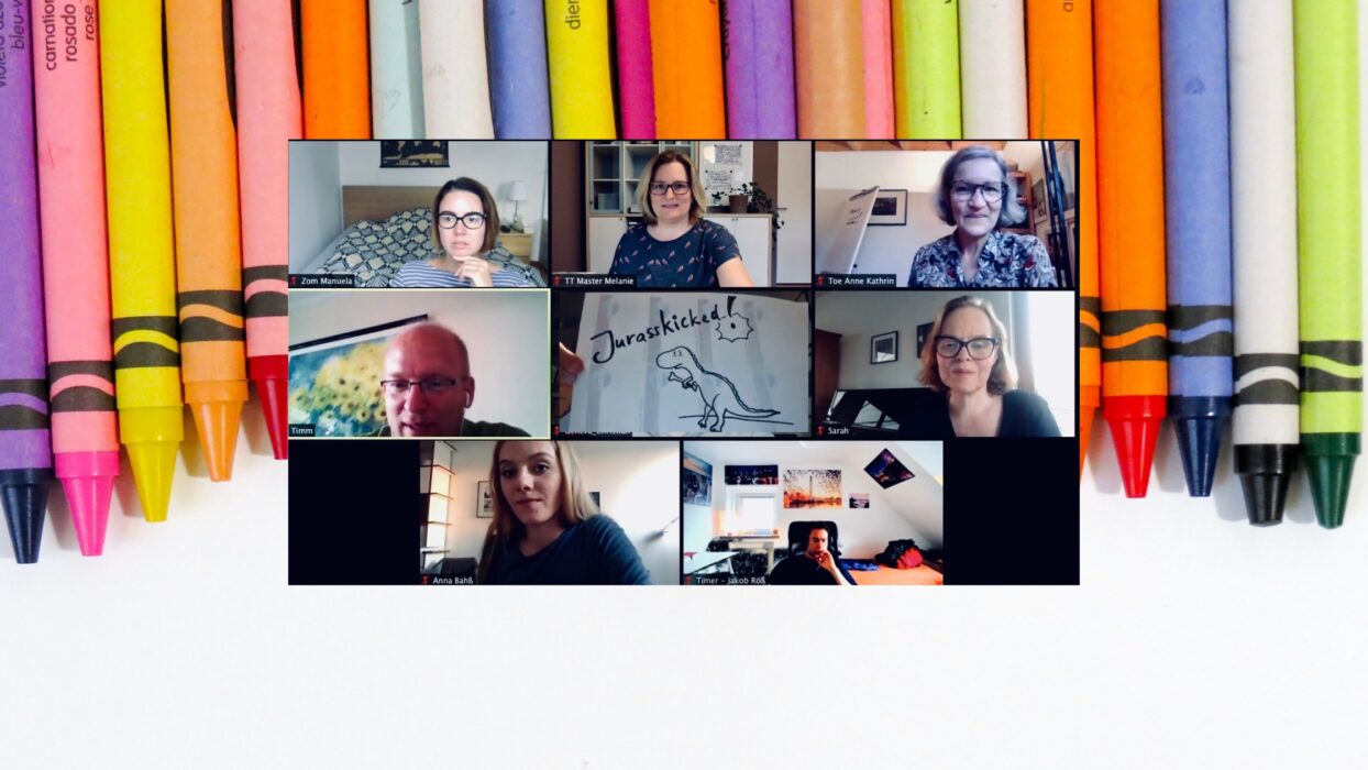 Grafik vor bunten Buntstiften mit einem Zoom-Konferenz-Raster von Toastmasters-Mitgliedern, darunter jemand mit einer Dinosaurier-Zeichnung „Jurasskicked!“.