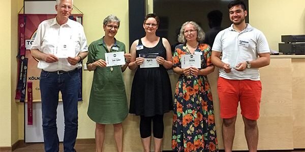 Fünf lächelnde Toastmasters aus Aachen stehen nebeneinander vor dem Toastmasters-Banner und halten ihre Urkunden in den Händen.