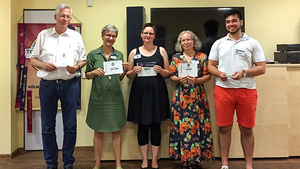 Fünf lächelnde Toastmasters aus Aachen stehen nebeneinander vor dem Toastmasters-Banner und halten ihre Urkunden in den Händen.