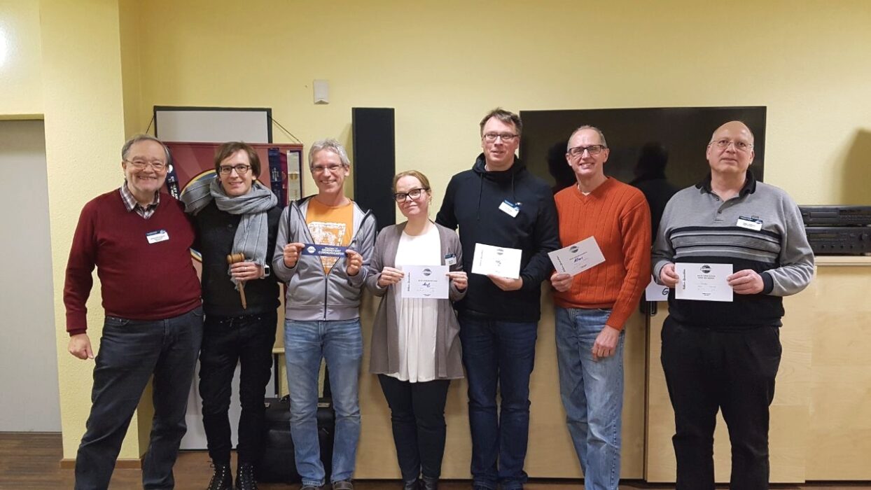 Sieben lächelnde Mitglieder der Kölner Sprechbar stehen nebeneinander und halten ihre Urkunden in den Händen.
