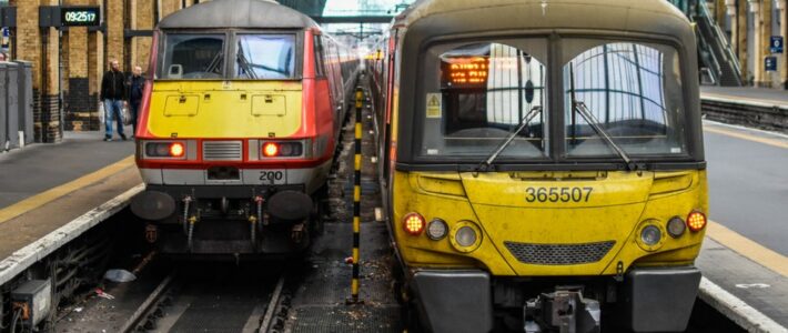 Zwei Züge stehen nebeneinander an einem Bahnsteig unter einer historischen Bahnhofshalle – Ankündigungsgrafik zum Motto "Bitte einsteigen".