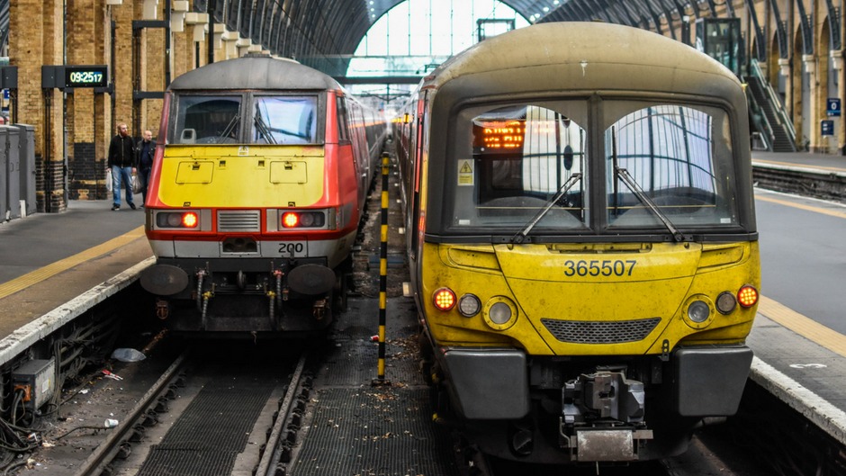 Zwei Züge stehen nebeneinander an einem Bahnsteig unter einer historischen Bahnhofshalle – Ankündigungsgrafik zum Motto "Bitte einsteigen".