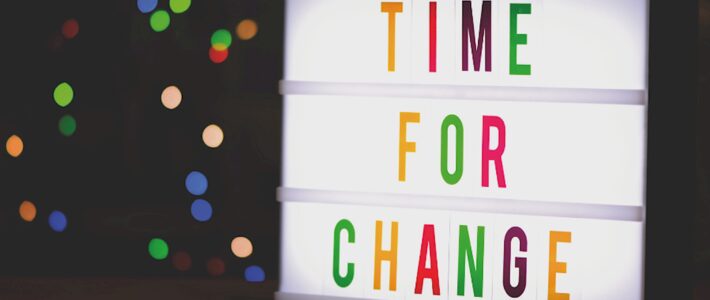 Eine beleuchtete Buchstabenbox zeigt bunt die Worte „Time for Change“, im dunklen Hintergrund funkeln unscharfe Lichter.