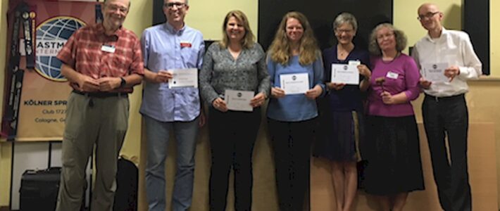 Sieben Mitglieder der Kölner Sprechbar stehen mit Urkunden vor dem Toastmasters-Banner.