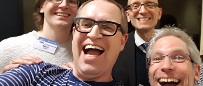 Vier lächelnde Mitglieder der Kölner Sprechbar posieren eng zusammen für ein Selfie in geselliger Runde.