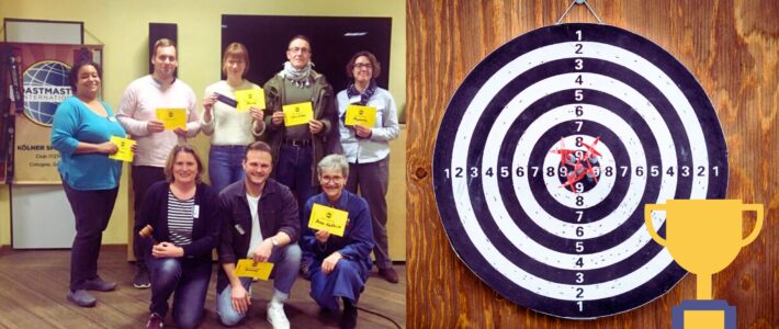 Erfolgreich ans Ziel Collage: acht Toastmasters-Mitglieder mit gelben Auszeichnungskarten links, daneben ein Dartboard mit Pfeilen im Zentrum und ein Pokal-Symbol.