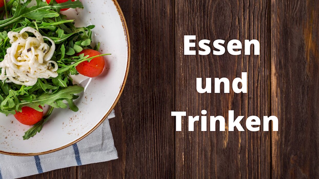 Teller mit Salat und Besteck auf einem Holztisch neben dem Schriftzug Essen und Trinken.