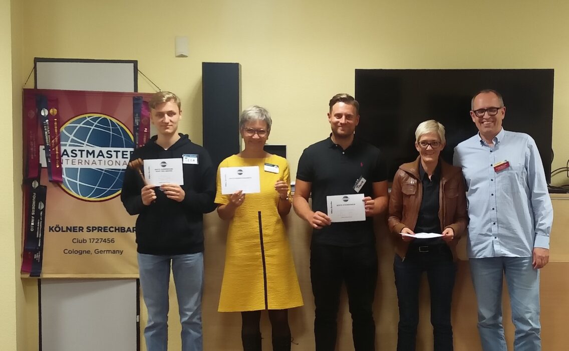 Fünf Teilnehmende stehen mit Urkunden vor dem Toastmasters-Banner.