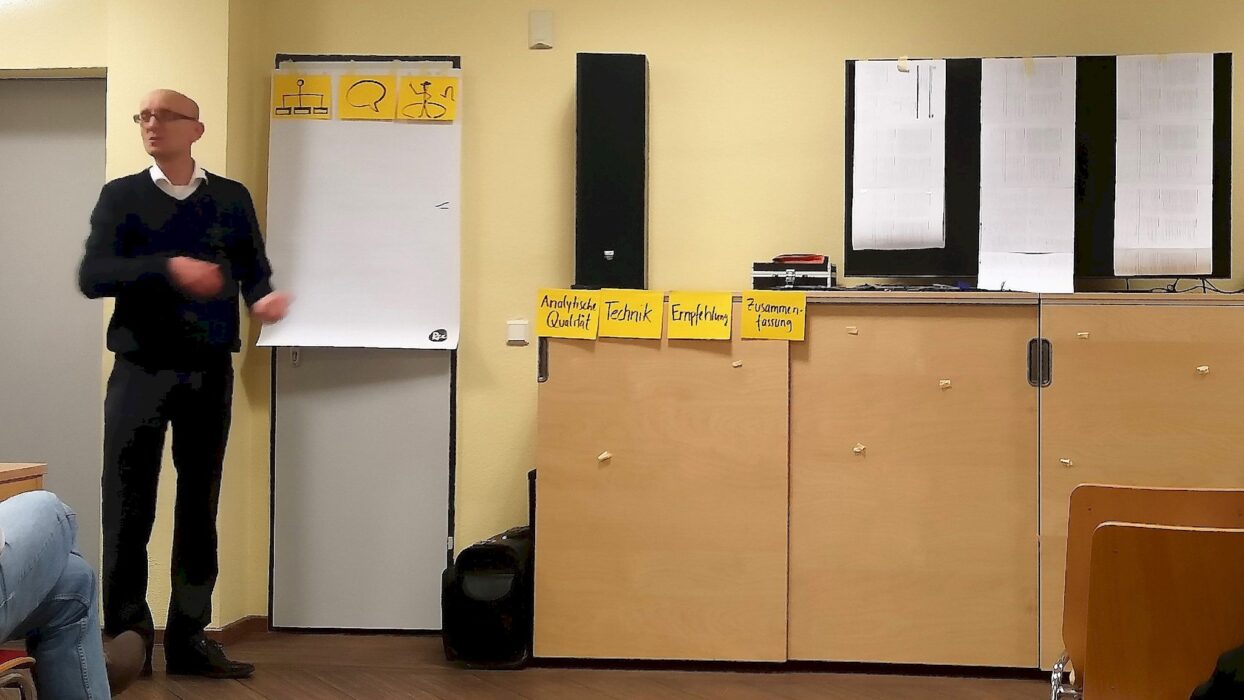 Redner erläutert Bewertungsstrukturen neben Flipchart und beschrifteten Karten.