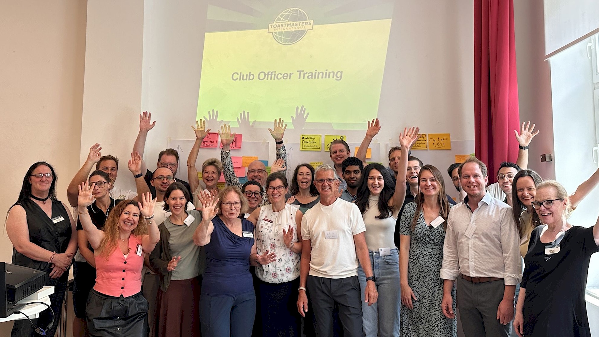 Gruppenfoto aller Teilnehmenden des Club Officer Training der Area A3, alle winken in die Kamera, im Hintergrund die Projektion „Club Officer Training“.