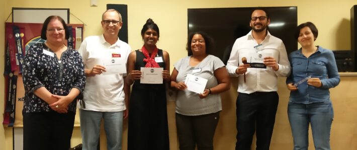 Sechs Teilnehmende stehen mit Urkunden und Hammer vor dem Toastmasters-Banner.