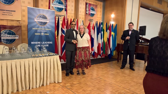 Andrea Sauerzweig schüttelt bei der Distrikt-Konferenz die Hand des Toastmasters-International-Präsidenten Balraj Arunasalam, im Hintergrund die Flaggen der teilnehmenden Länder.