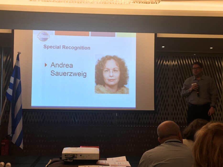 Präsentationsfolie "Special Recognition" mit Foto und Namen von Andrea Sauerzweig, im Hintergrund ein Redner auf der Bühne der Distrikt-Konferenz.