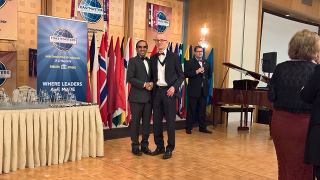 Christian Bahß schüttelt bei der Distrikt-Konferenz die Hand des Toastmasters-International-Präsidenten Balraj Arunasalam, im Hintergrund die Flaggen der teilnehmenden Länder.