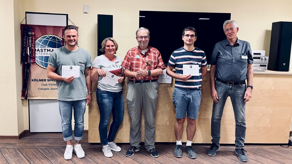 Fünf lächelnde Toastmasters-Mitglieder stehen nebeneinander, drei von ihnen halten ihre Auszeichnungsurkunden in den Händen.