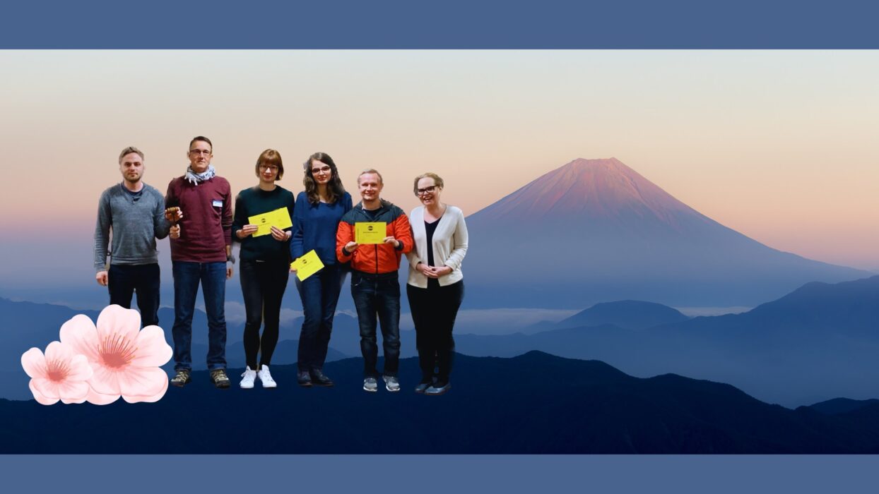 Sechs Toastmasters-Mitglieder mit gelben Auszeichnungskarten stehen vor einer Fotomontage mit dem Fuji und Kirschblüten.