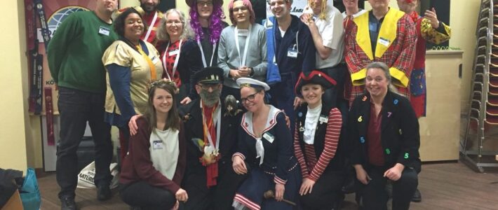 Bunt kostümierte Mitglieder der Kölner Sprechbar feiern gemeinsam Karneval, mit Orden und Medaillen geschmückt.