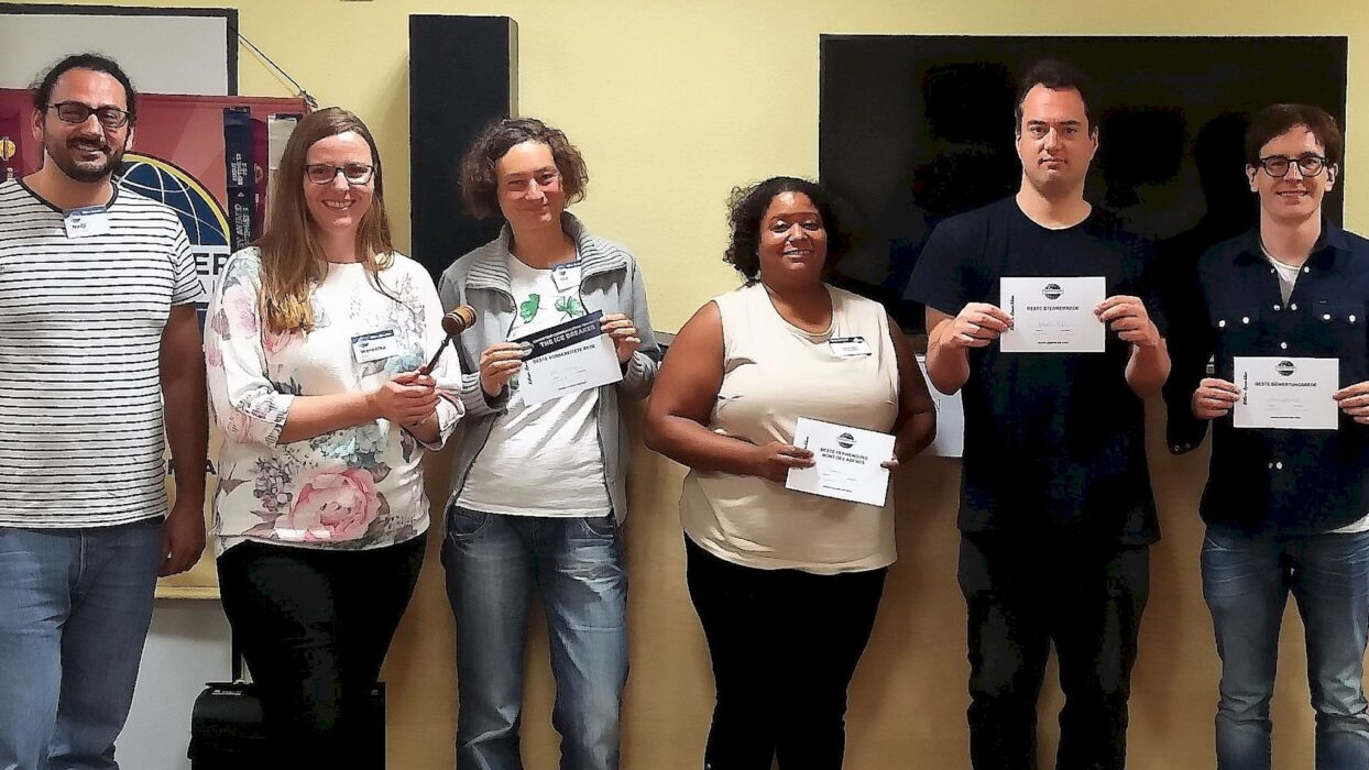 Sechs Teilnehmende stehen mit Urkunden und Hammer vor dem Toastmasters-Banner.