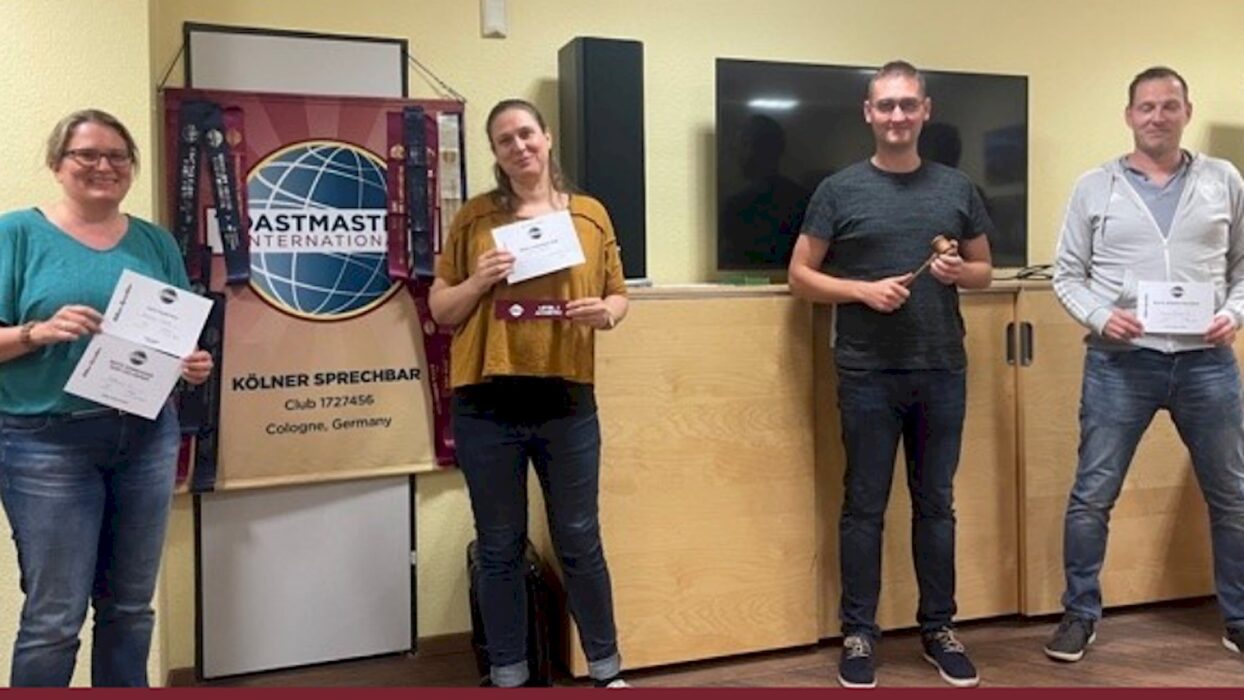 Vier Teilnehmende stehen mit Urkunden und Hammer vor dem Toastmasters-Banner.