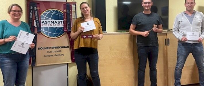 Vier Teilnehmende stehen mit Urkunden und Hammer vor dem Toastmasters-Banner.