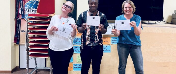 Lieblingslektüre Drei lächelnde Toastmasters-Mitglieder halten ihre Auszeichnungsurkunden, im Hintergrund Klebezettel mit Lieblingsbuchtiteln.