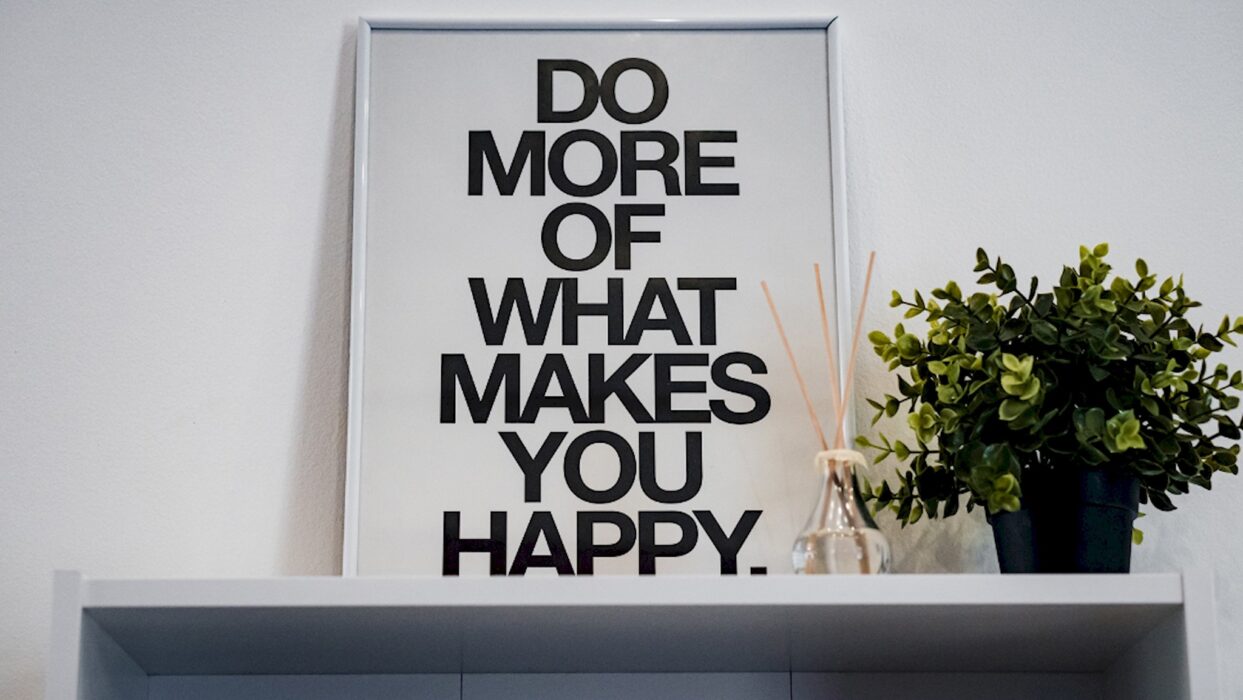 Gerahmtes Poster mit dem englischen Motivationsspruch „Do more of what makes you happy“ neben einer grünen Pflanze.
