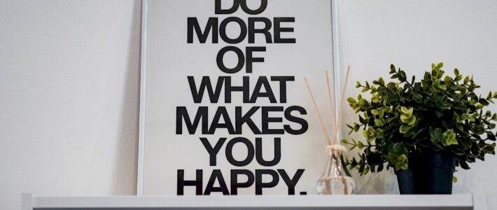 Gerahmtes Poster mit dem englischen Motivationsspruch „Do more of what makes you happy“ neben einer grünen Pflanze.