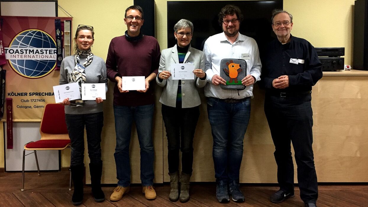 Fünf Mitglieder der Kölner Sprechbar stehen vor dem Toastmasters-Banner und halten Urkunden.