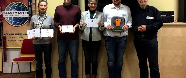 Fünf Mitglieder der Kölner Sprechbar stehen vor dem Toastmasters-Banner und halten Urkunden.