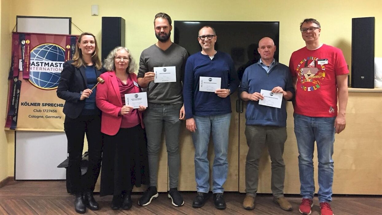 Sechs Teilnehmende stehen mit Urkunden und Hammer vor dem Toastmasters-Banner.