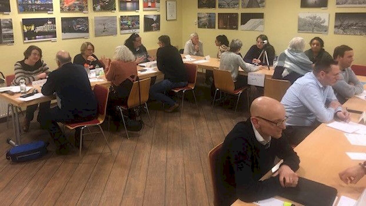 Teilnehmende eines Living-Library-Abends sitzen sich in kleinen Gesprächsgruppen an mehreren Tischen gegenüber.