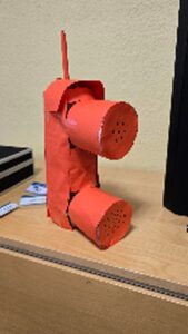 Ein aus rotem Karton selbstgebasteltes Spielzeugtelefon mit Hörer und Wählscheibe steht auf einem Holztisch.