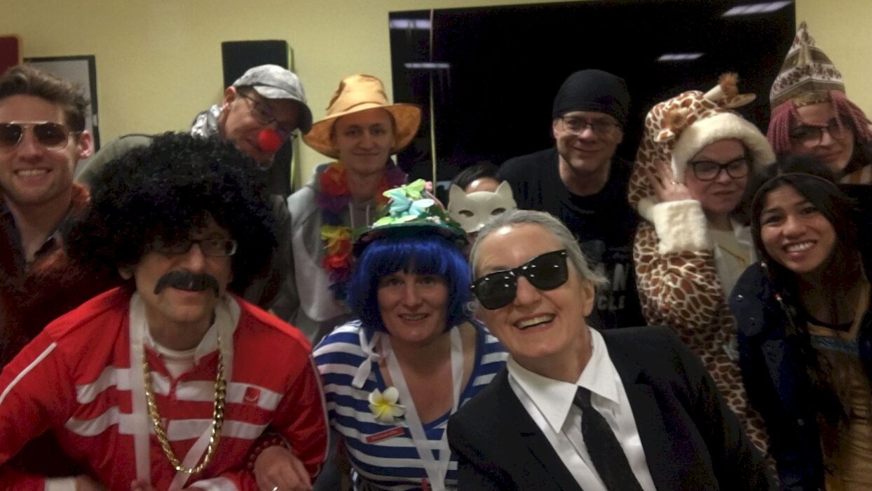 Eine Gruppe kostümierter Toastmasters-Mitglieder und Gäste beim Karneval, darunter Kostüme wie Giraffe, Katze und Karl Lagerfeld.