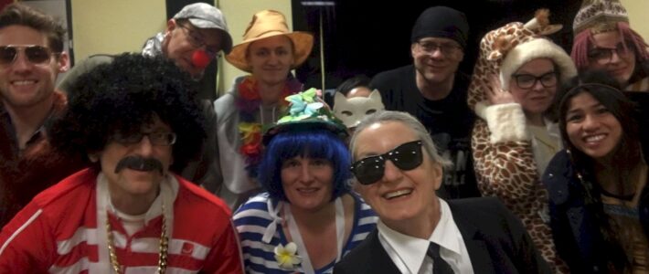 Eine Gruppe kostümierter Toastmasters-Mitglieder und Gäste beim Karneval, darunter Kostüme wie Giraffe, Katze und Karl Lagerfeld.
