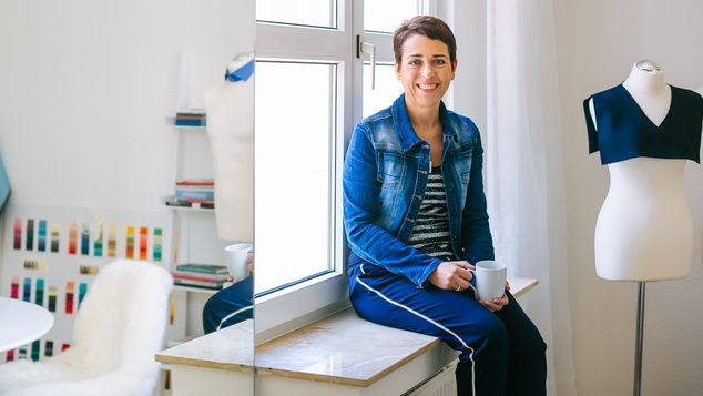 Claudia Reuschenbach sitzt in einem hellen Stilberatungsraum neben einer Schneiderpuppe.