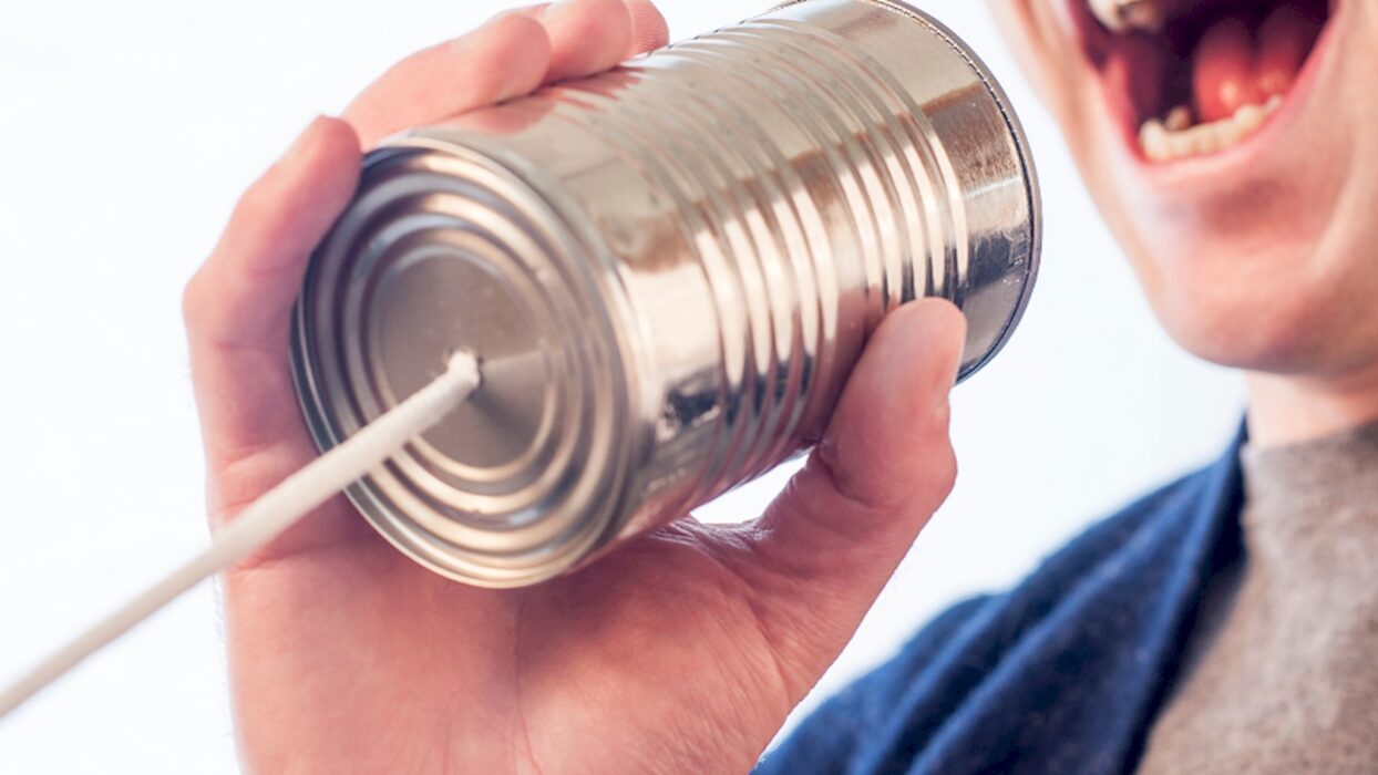 Person spricht in ein Dosentelefon und hält die Schnur vor weißem Hintergrund gespannt.