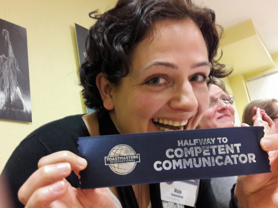 Maja hält lächelnd ihr Abzeichen "Halfway to Competent Communicator" in die Kamera.