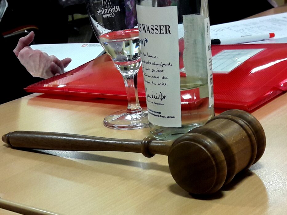 Sektglas, Wasserflasche mit Gedicht-Etikett und Präsidentenhammer auf dem Tisch der Kölner Sprechbar.