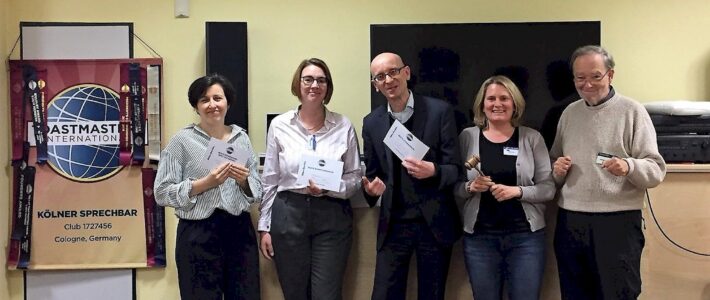 Fünf Teilnehmende stehen mit Urkunden und Hammer vor dem Toastmasters-Banner.