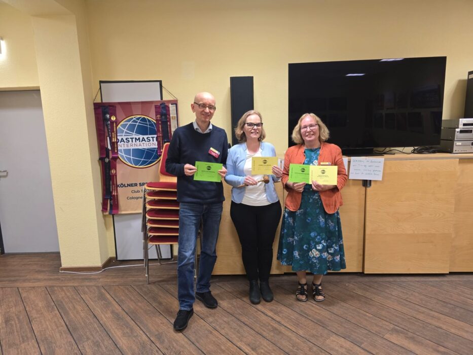 Drei Preisträger des Abends mit Urkunden und dem Hammer vor dem Toastmasters-Banner