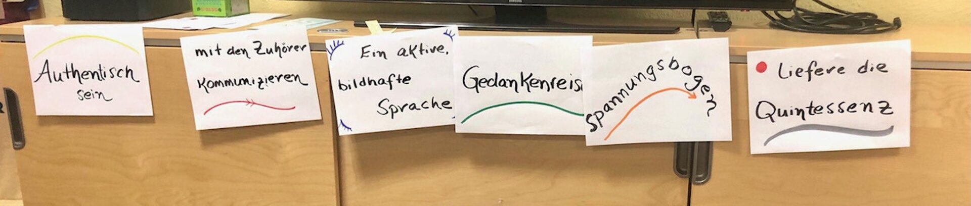 Beschriftete Papierstreifen zu Rhetorik und Redestruktur liegen auf einer braunen Fläche.